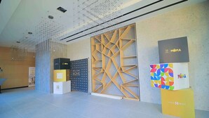 A modern interior with a geometric wall design, a suspended ceiling, and branded display boxes. - High-End 1BR in Secure Tower | Parking | Mamak (Tel Aviv-Yafo)