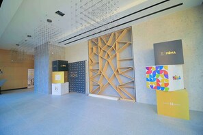 A modern interior with a geometric wall design, a suspended ceiling, and branded display boxes. - High-End 1BR in Secure Tower | Parking | Mamak (Tel Aviv-Yafo)