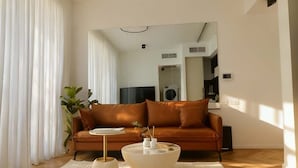 A living room with a brown sofa, a round coffee table, and a white rug. - High-End 1BR in Secure Tower | Parking | Mamak (Tel Aviv-Yafo)