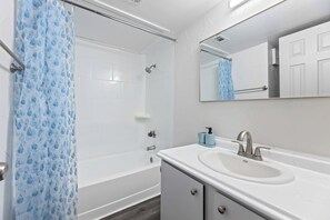 A bathroom with a bathtub, a sink, a mirror, and a shower curtain. - Modern Arlington Escape • Stadium 8 Min Away (Arlington)