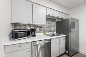 A kitchen with white cabinets, a stainless steel refrigerator, a microwave, and a dishwasher. - Steps from AT&T Stadium | Parking (Arlington)