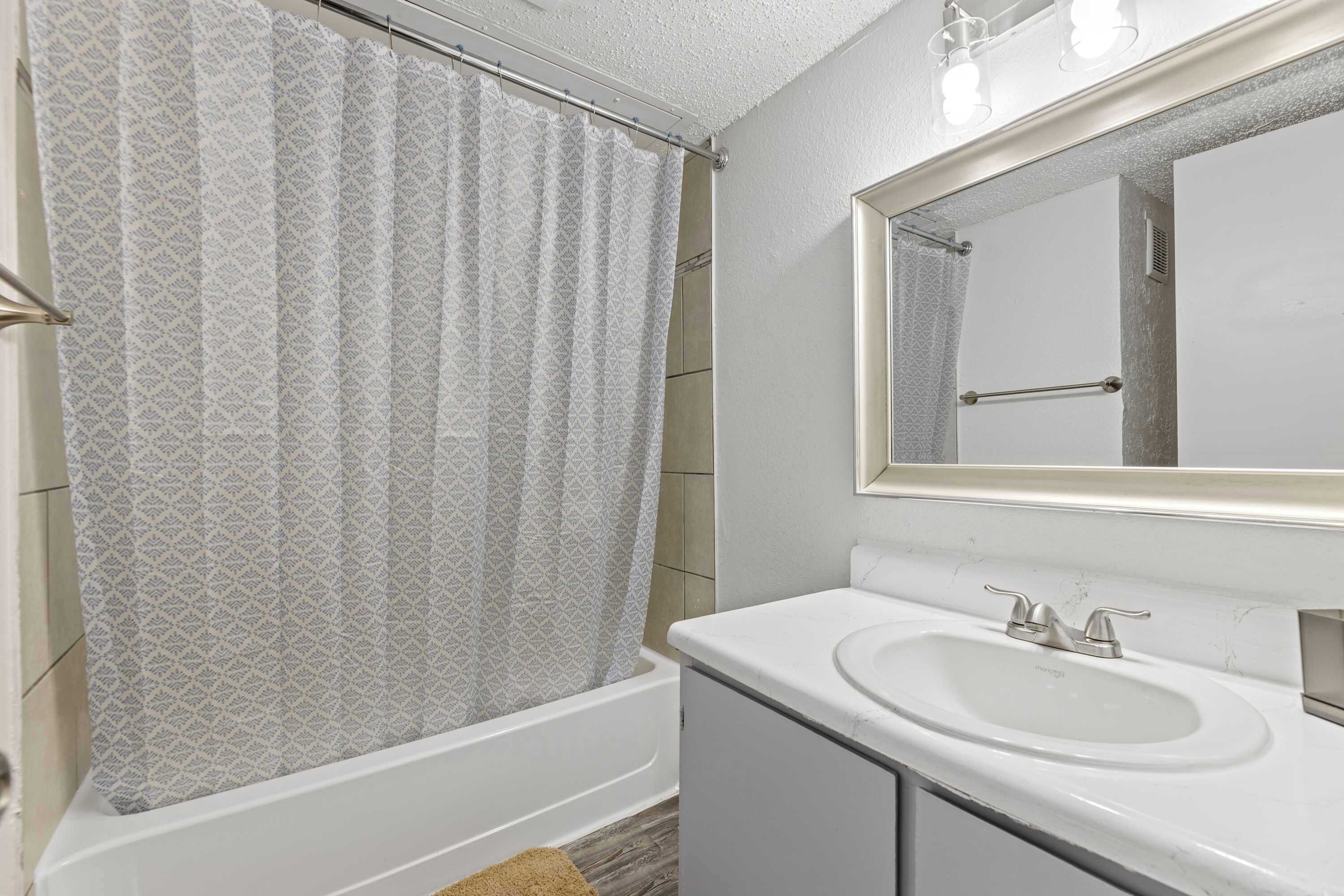 A bathroom with a bathtub, a sink, and a mirror.