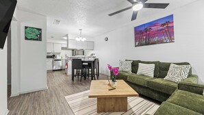 A modern living room with a green sofa, a wooden coffee table, and a cityscape painting. - City Comfort • 2BR • Stadium Within Walking (Arlington)