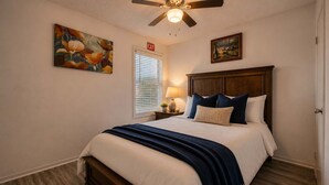 A bedroom with a bed, a ceiling fan, a nightstand with a lamp, and artwork on the walls. - City Comfort • 2BR • Stadium Within Walking (Arlington)