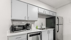A modern kitchen with white cabinets, a stainless steel dishwasher, a microwave, a coffee maker, and a refrigerator. - City Comfort • 2BR • Stadium Within Walking (Arlington)
