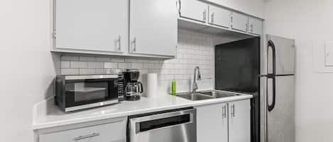 Una cocina moderna con armarios blancos, lavavajillas de acero inoxidable, microondas, cafetera y refrigerador.