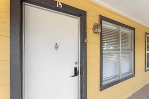 Ein Gebäude mit einer weißen Tür, einem Fenster mit Rollläden und der Hausnummer 15 darüber.