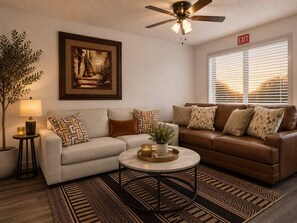 A living room with a sofa, a coffee table, a lamp, a plant, and a ceiling fan. - AT&T Stadium Retreat | Free Parking (Arlington)