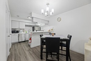A compact kitchen with white cabinets, a microwave, and a dining area with a table and chairs. - AT&T Stadium Retreat | Free Parking (Arlington)