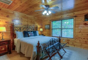 A wooden cabin bedroom with a bed, two bedside tables, a ceiling fan, and a window with blinds. - New Moon (Sevierville)