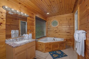 A wooden cabin bathroom with a sink, vanity, bathtub, and a mirror with lights. - New Moon (Sevierville)