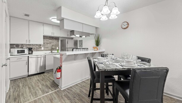 Una cocina moderna con armarios blancos, un microondas y una zona de comedor con una mesa de mármol y sillas negras.