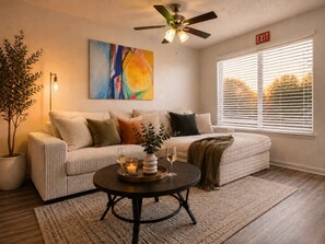 Ein Wohnzimmer mit einer Couch, einem Couchtisch, einem Deckenventilator, einem Gemälde und einem Fenster mit Jalousien.