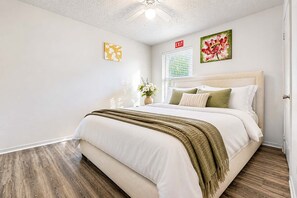 Ein Schlafzimmer mit Bett, Deckenventilator, Fenster mit Jalousien und einer Tür.
