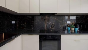A modern kitchen with a black marble backsplash, white cabinets, and a built-in dishwasher. - Comfortable Studio with a Balcony | Near Westfield Mokotów (Warszawa)