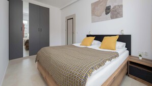 A bedroom with a bed, a wardrobe, a bedside table, and a wall-mounted artwork. - Comfortable Studio with a Balcony | Near Westfield Mokotów (Warszawa)