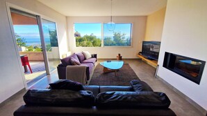 Ein modernes Wohnzimmer mit einer Couch, einem Couchtisch, einem Fernseher und großen Fenstern mit Blick.
