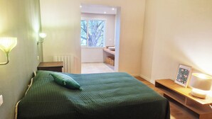 Ein Schlafzimmer mit Bett, Nachttischlampe und Blick auf ein Badezimmer.