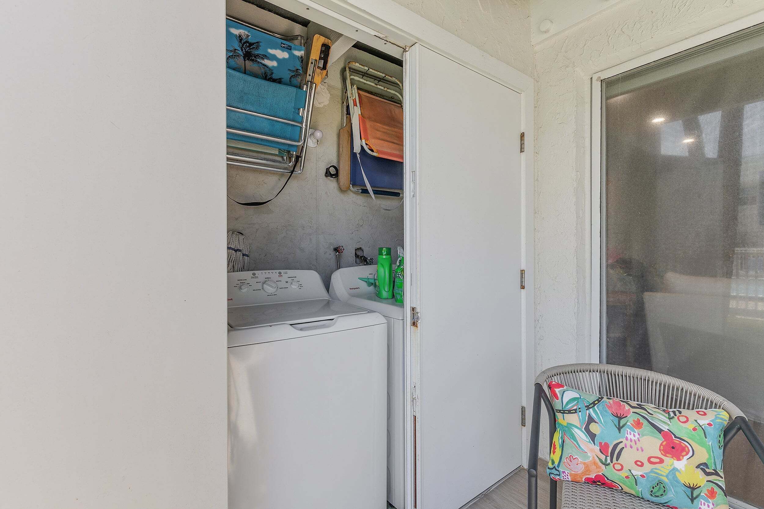 A laundry area with a washing machine, drying racks, and a chair with a colorful cushion.