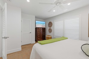 A bedroom with a bed, a television, a ceiling fan, and a view of the beach through the window. - Relaxing King Suite With Poolside Patio & Partial Ocean Views (New Smyrna Beach)