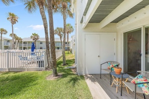 A covered outdoor area with a table and chairs, palm trees, and a view of other buildings. - Relaxing King Suite With Poolside Patio & Partial Ocean Views (New Smyrna Beach)
