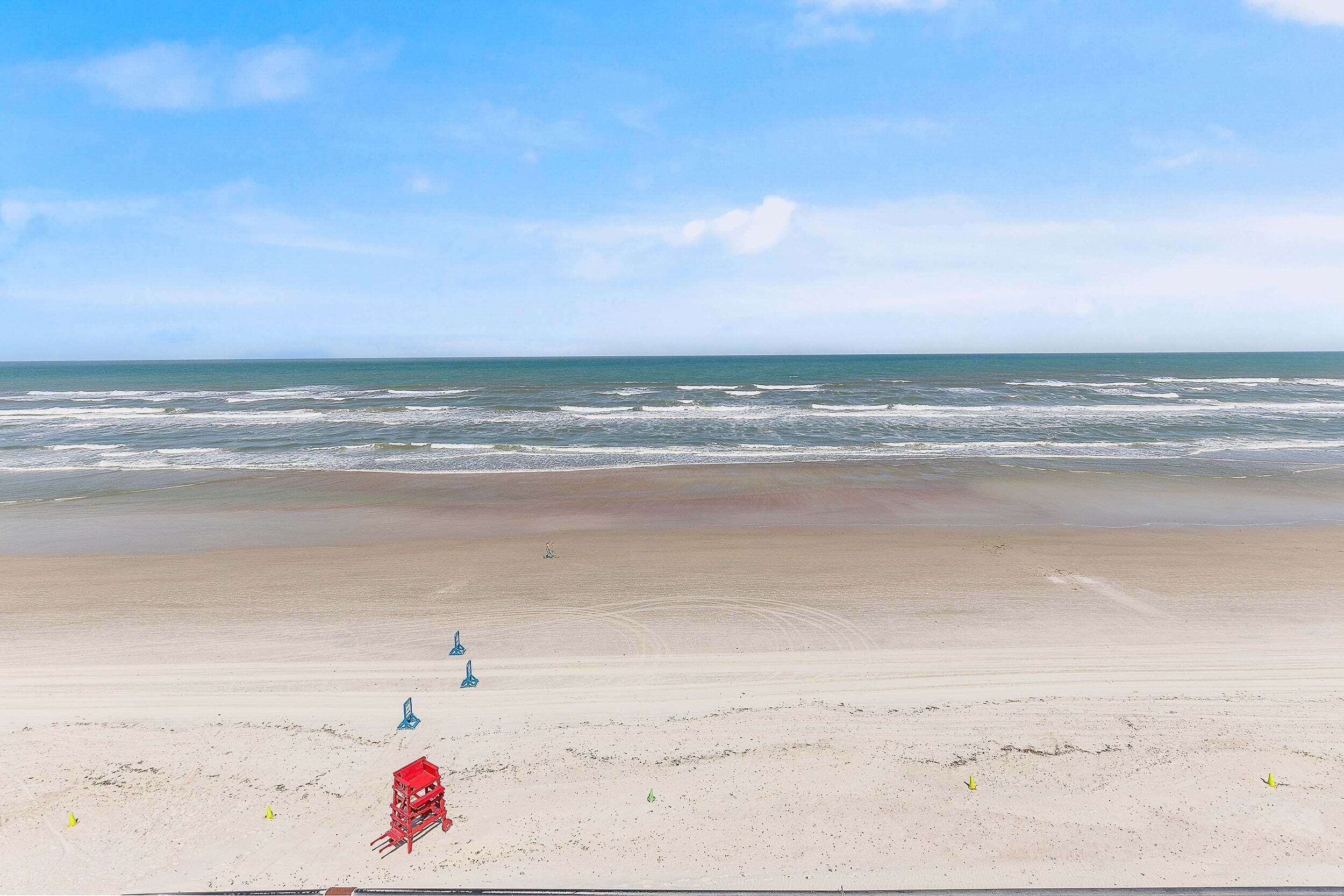A beach with a lifeguard tower, a red lifeguard chair, and yellow cones on the sand.