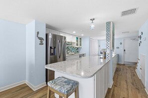 A modern kitchen with a marble countertop, stainless steel appliances, and a wooden floor. - Pelican D-305 (New Smyrna Beach)