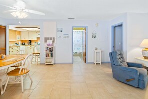 Ein geräumiger Wohnbereich mit Esstisch, Stühlen, einem blauen Sessel und Deckenventilator.