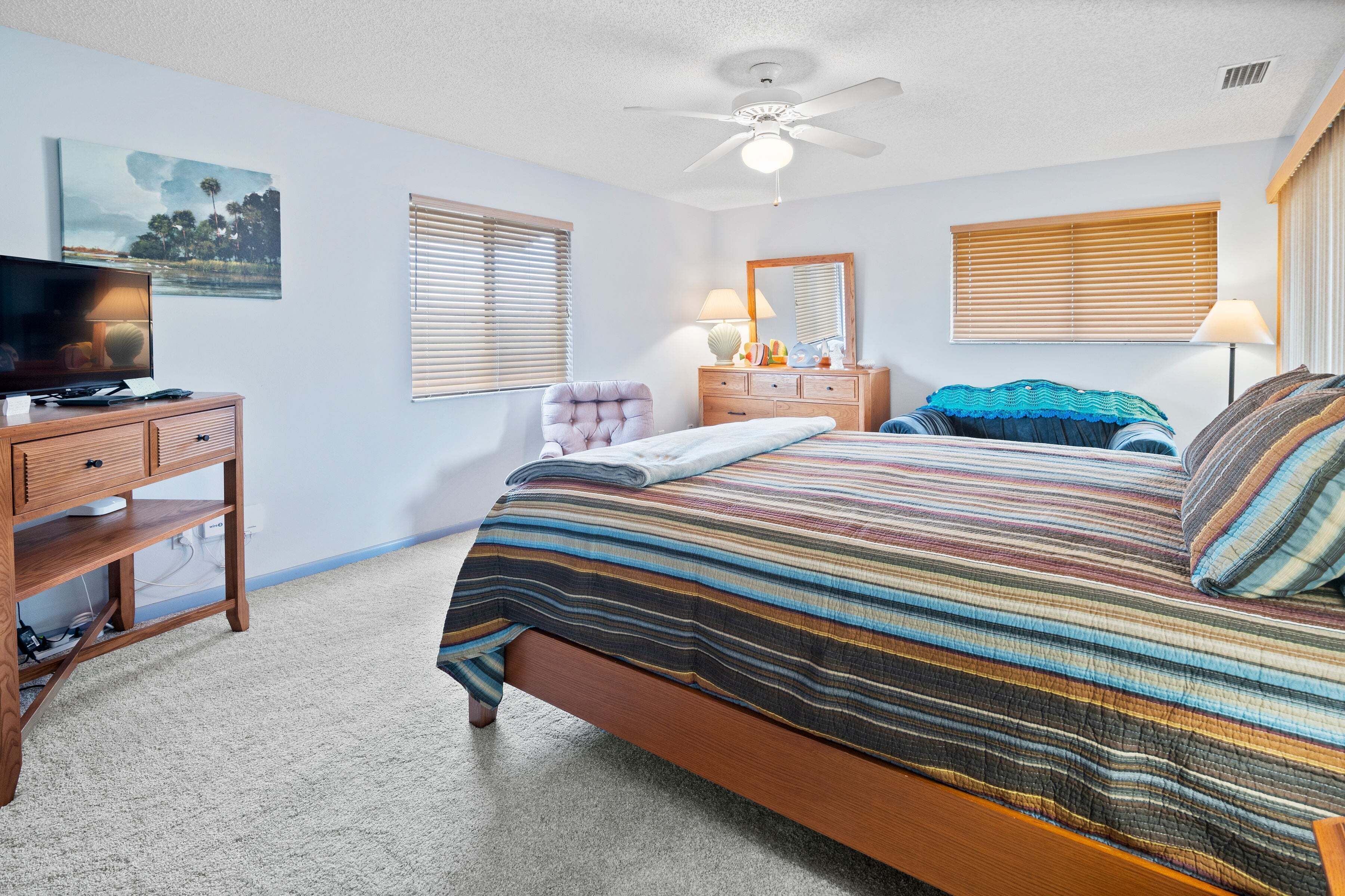 A bedroom with a bed, a wooden dresser, a television, and a ceiling fan.