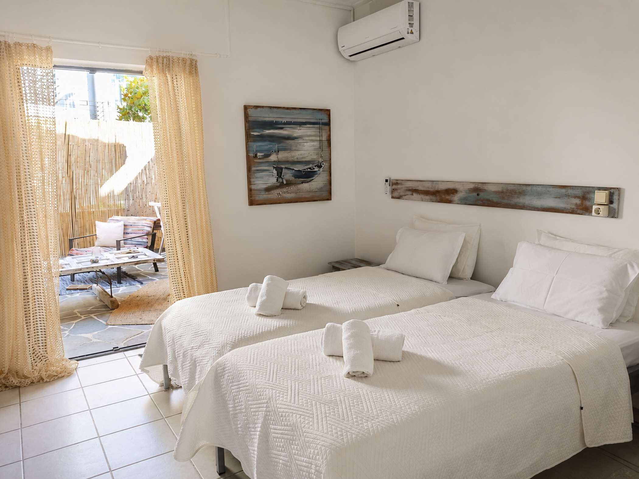Ein Hotelzimmer mit zwei Betten, einem Gemälde, einer Klimaanlage und Blick ins Freie.