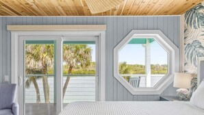 A bedroom with a bed, a chair, a window, and a view of palm trees. - La De Dah (Edgewater)