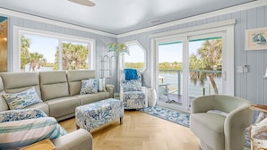 A room with a sofa, armchairs, and a view of palm trees through large windows. - La De Dah (Edgewater)
