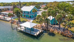 A coastal property with a dock, a large house with a blue roof, and surrounding palm trees. - La De Dah (Edgewater)