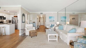 A spacious living area with a white sofa, a coffee table, and a kitchen area with modern appliances. - Updated Oceanview Retreat With Pools, Pickleball & Direct Beach Access (New Smyrna Beach)