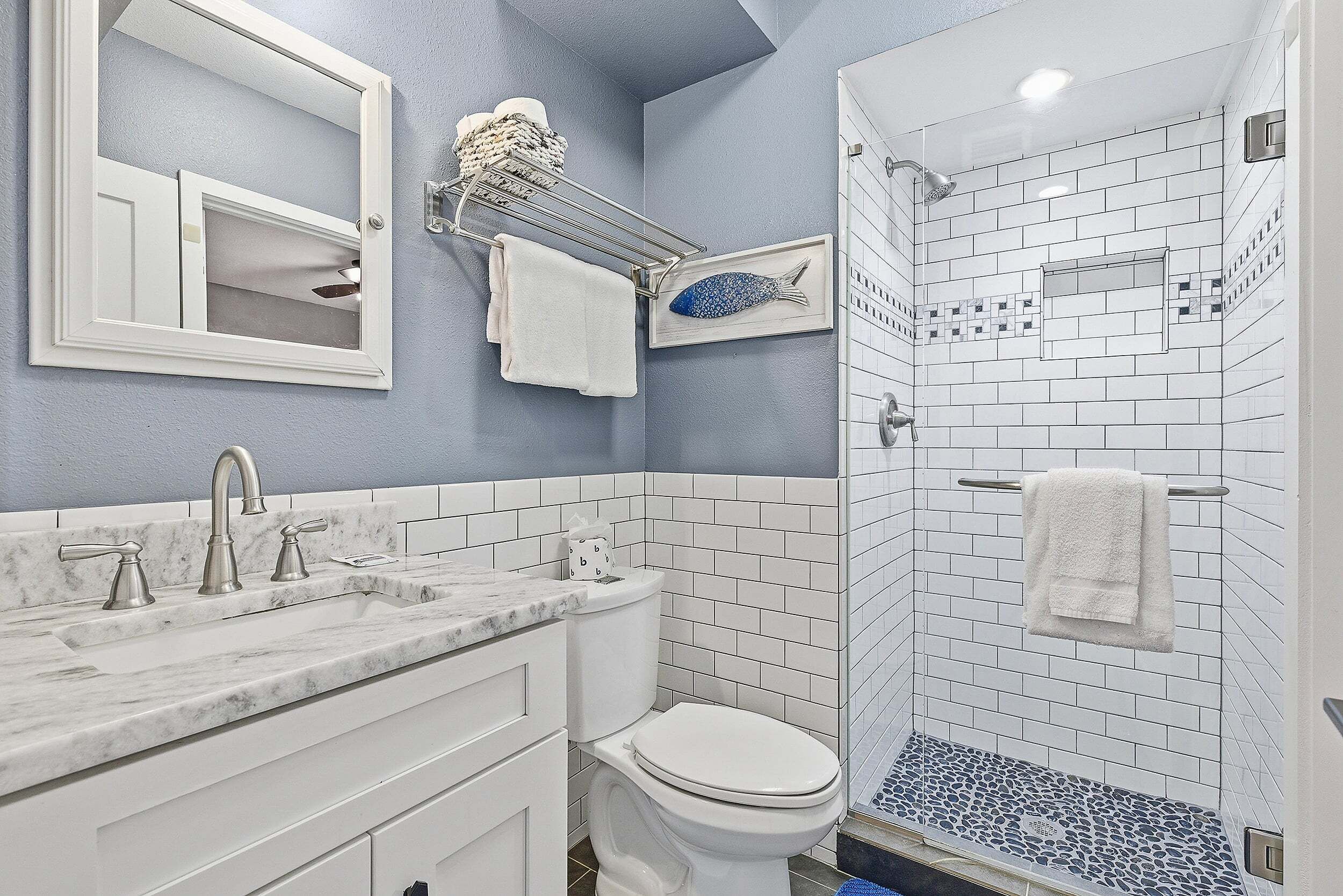 A bathroom with a marble sink, a toilet, a shower with white tiles, and a towel rack.