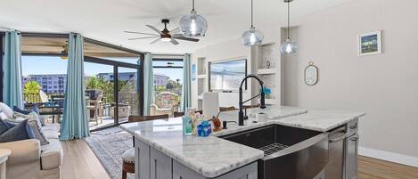 A modern kitchen with a large island, a dining area with a view, and a ceiling fan.