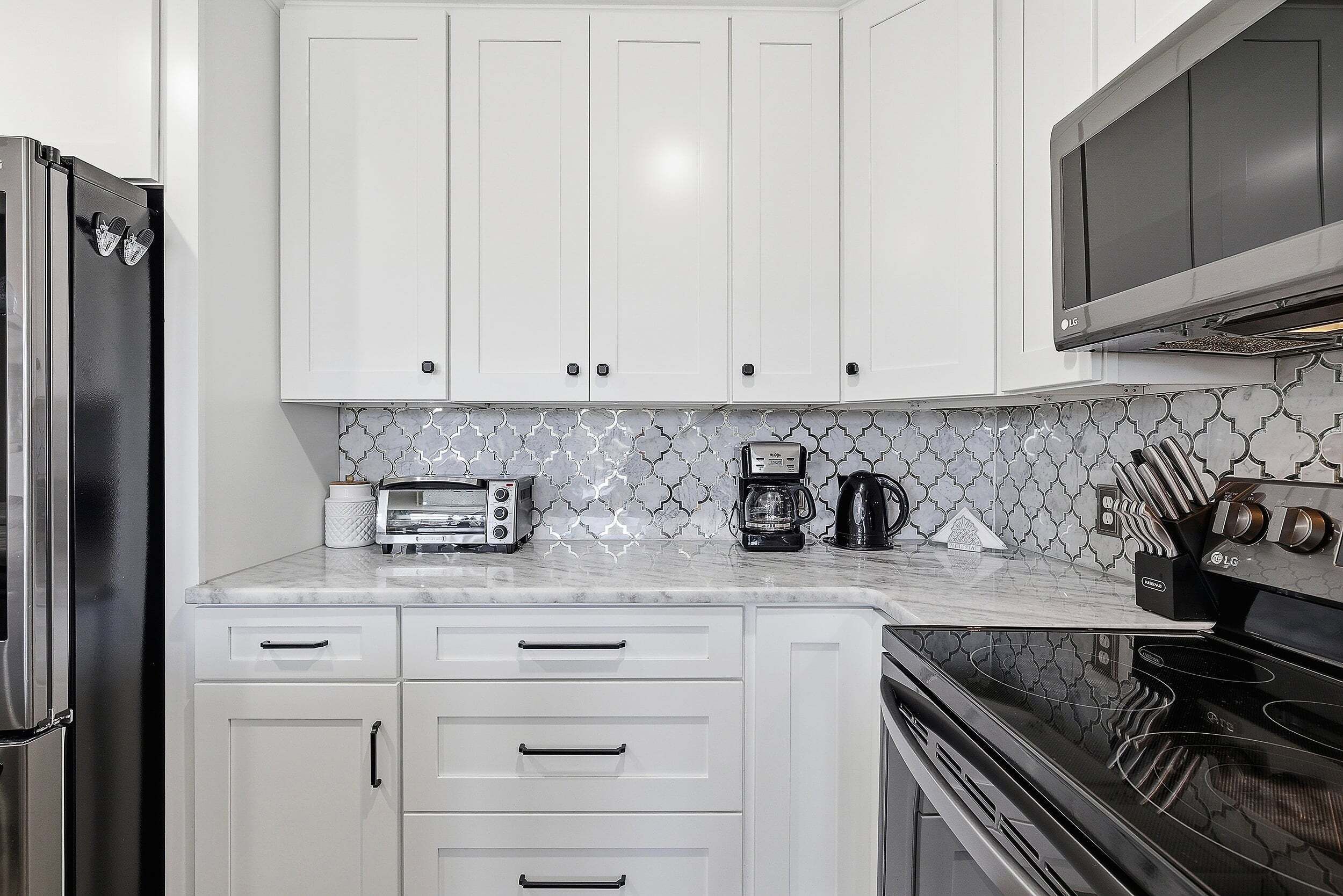 A kitchen with white cabinets, a black refrigerator, a microwave, a coffee maker, and a stove.