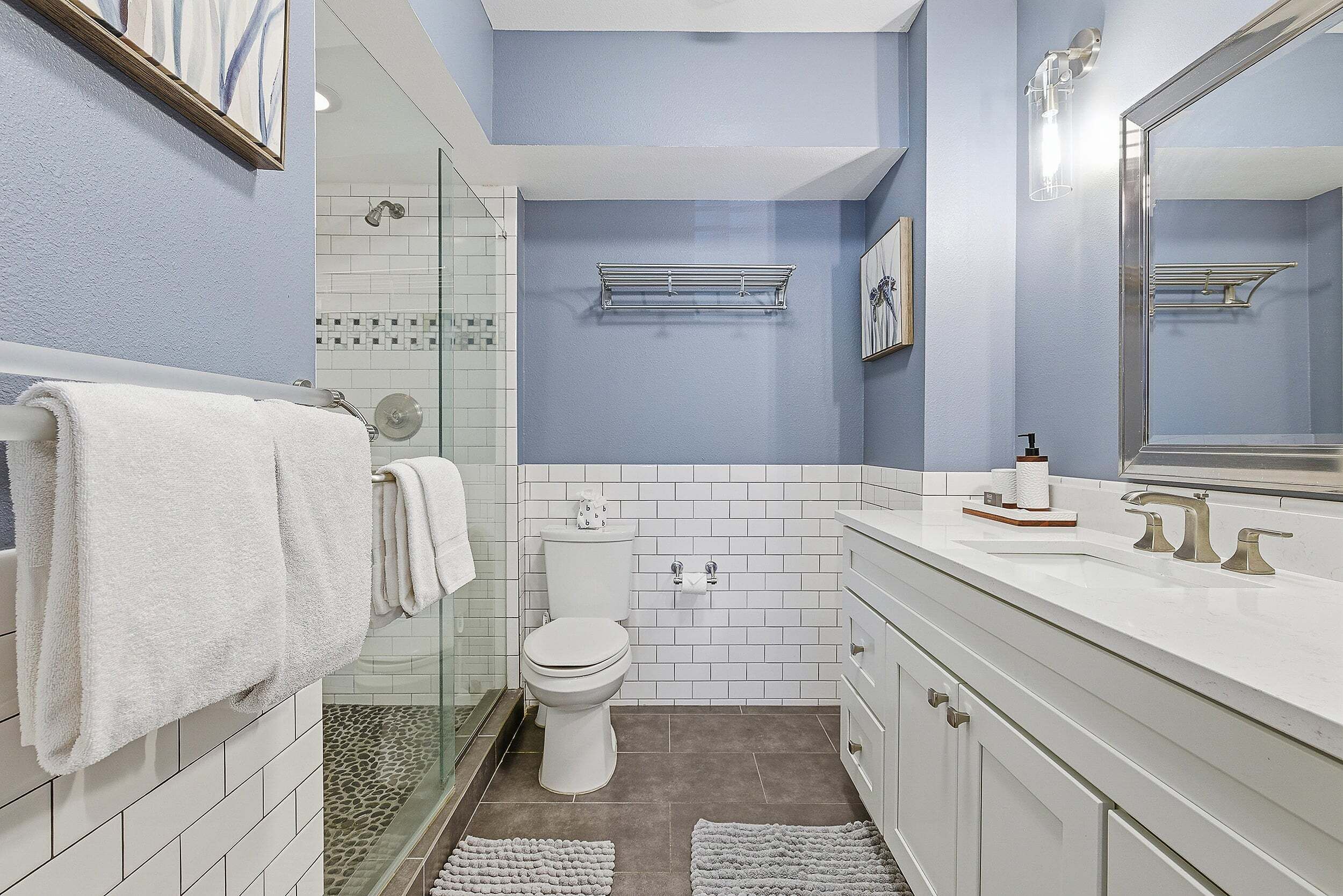 A bathroom with a glass shower, white tiles, a white toilet, and a white sink with a mirror.