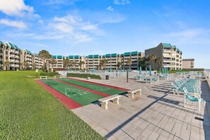 Ein Innenhof mit einem Shuffleboard-Spielfeld, Liegestühlen und einem Gebäude mit mehreren Balkonen.
