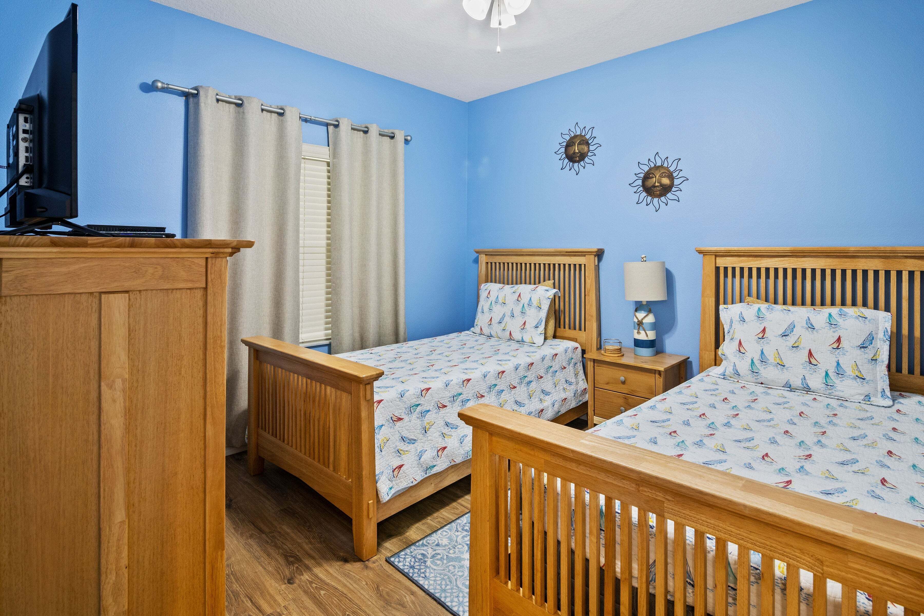 A room with two wooden beds, a desk, a television, and a window with curtains.