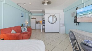 Una habitació amb un llit, un sofà vermell, una zona de cuina i vista a l'oceà per una finestra.