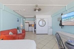 A room with a bed, a red sofa, a kitchen area, and a view of the ocean through a window. - Hawaiian Inn 332 (Daytona Beach Shores)