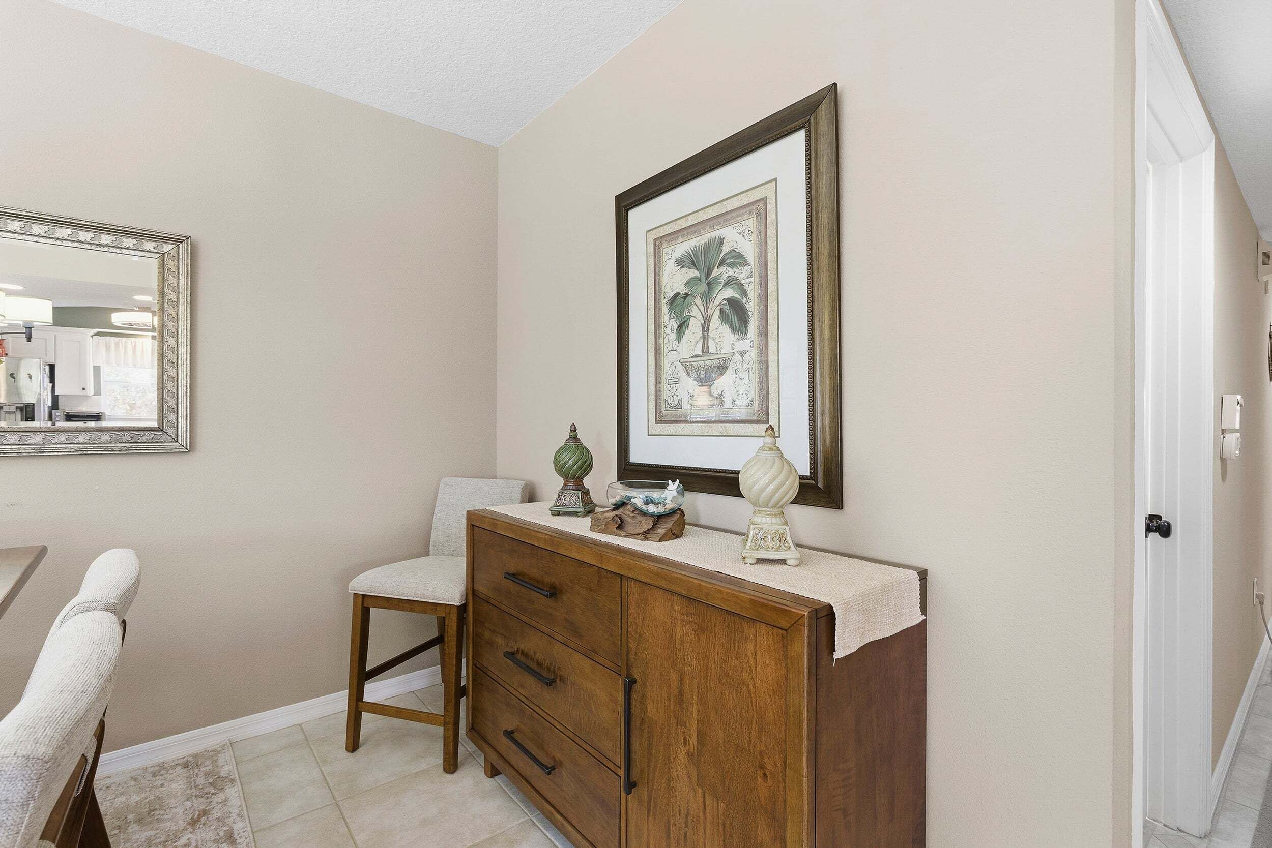 A bathroom with a wooden vanity, a mirror, a framed picture, and a small decorative item on the counter.