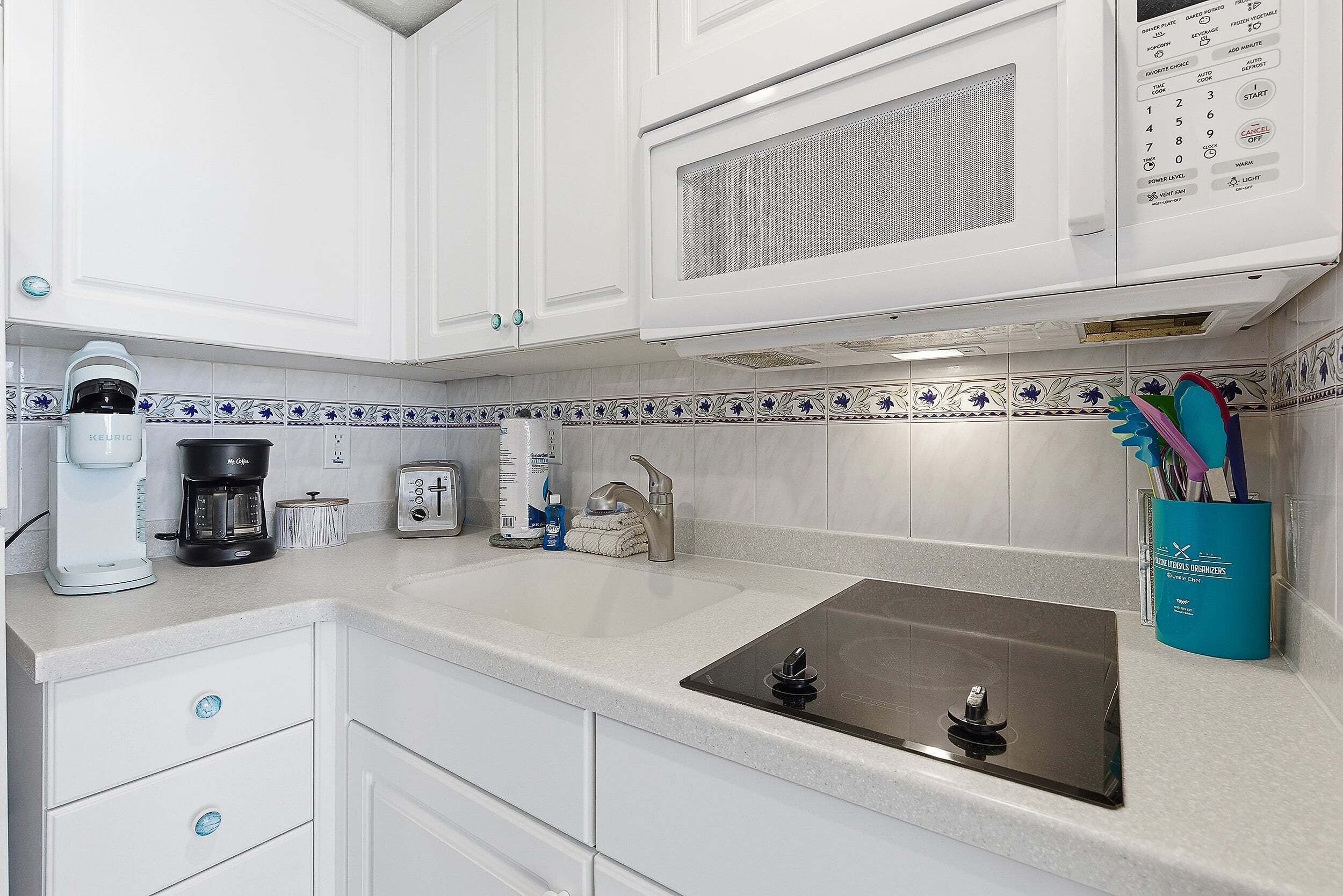 A kitchen with white cabinets, a coffee maker, a toaster, a microwave, and a sink.