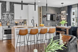 A modern kitchen with white cabinets, a stainless steel stove, and a bar area with stools. - Rooftop Oasis - Hot Tub, Nashville City Views (Nashville)
