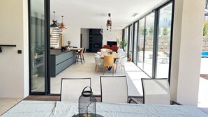 Un intérieur moderne comprenant un coin repas, une cuisine et de grandes portes-fenêtres coulissantes donnant sur un espace extérieur.