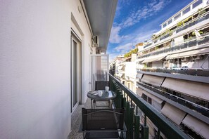 En balkon med et bord og stole, et vindue samt udsigt til omkringliggende bygninger.