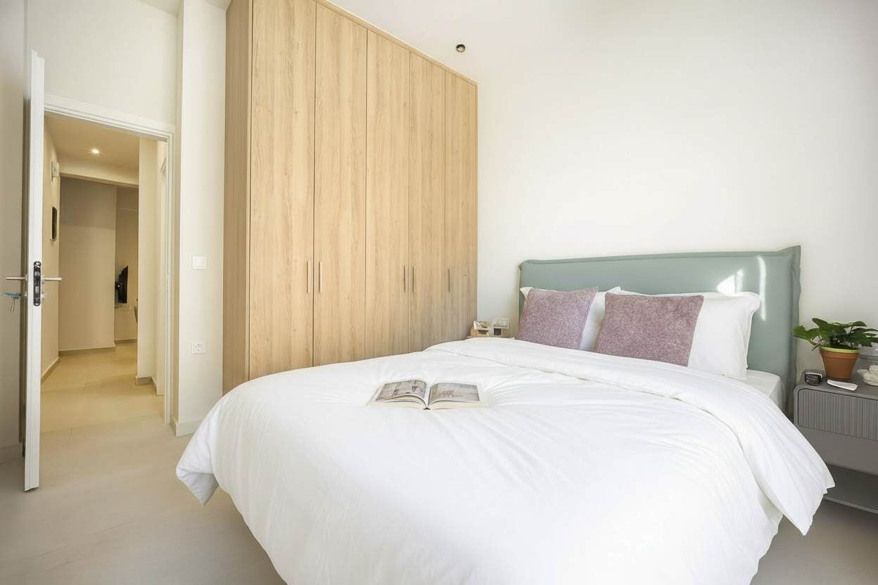 A bedroom with a bed, a wardrobe, a bedside table with a lamp, and a potted plant.
