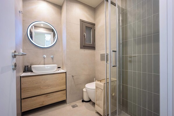 Un baño moderno con un espejo redondo, un lavabo, un inodoro y una cabina de ducha con mampara de vidrio.