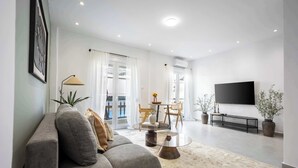Ett modernt vardagsrum med en grå soffa, ett runt soffbord, en platt-TV och en matplats med ett bord och stolar.